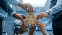 Diverse business team assembling wooden blocks with people icons in circle formation, symbolizing teamwork, collaboration, and human resources management for corporate projects.
