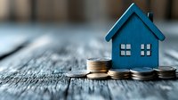 Small blue wooden house model placed on stack of coins against rustic wooden background, representing real estate investment, mortgage, and property finance.