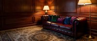 Luxurious leather chesterfield sofa with colorful pillows in elegant wood-paneled library room with warm lighting and ornate carpet for interior design.