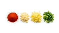Four colorful food ingredients arranged in neat piles on white background showing red paprika powder, diced onions, pasta and chopped green onions for cooking.