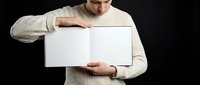 Young man in beige sweater holding blank white sign board against black background for advertising mockup and promotional display purposes.