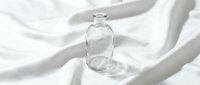 Empty glass bottle with dropper cap on white fabric with soft shadows, suitable for cosmetics, skincare, perfume, and essential oil product packaging design.