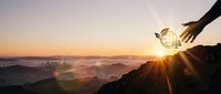 Silhouetted hand holding glowing globe above misty valley at sunrise, symbolizing environmental stewardship and global sustainability vision for eco-conscious projects.