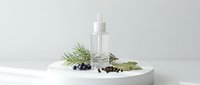 Natural skincare serum bottle with rosemary herbs and juniper berries on white surface for organic beauty product marketing and cosmetic branding.