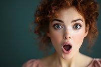 Young Caucasian woman with curly ginger hair and bright blue eyes expressing surprise with open mouth against dark green background. Close up portrait showing genuine emotion.