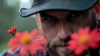 Bearded Caucasian man in black cap photographed through vibrant red daisy flowers, creating mysterious atmospheric portrait with shallow depth of field and bokeh effect.