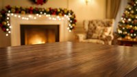 Empty wooden table surface with blurred Christmas living room background featuring fireplace, decorated tree and festive garland for holiday product display.