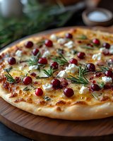Gourmet pizza topped with cranberries, goat cheese and fresh rosemary herbs on wooden board. Artisan flatbread with seasonal toppings for holiday dining and cooking.
