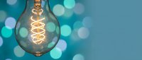 Vintage Edison bulb with warm spiral filament glowing against turquoise background with soft bokeh lights for creative lighting and electrical concepts.