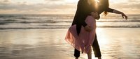 Romantic couple embracing on beach at sunset with golden light reflecting on wet sand and ocean waves creating intimate silhouette moment for love and relationship concepts.
