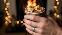 Hot chocolate with marshmallows held in hands by cozy fireplace with warm bokeh lights creating festive winter atmosphere for holiday celebrations.