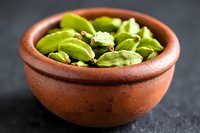Fresh green cardamom pods in traditional clay bowl on dark background, aromatic spice ingredient for cooking and flavoring beverages and desserts.