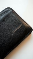 Black leather wallet corner detail showing textured grain surface and stitched edges on neutral background for business and finance concepts.
