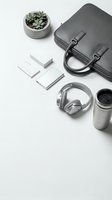Modern business workspace with gray leather briefcase, wireless headphones, coffee cup, succulent plant and white business cards on clean white background.