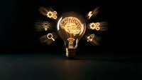 Glowing light bulb with brain inside surrounded by innovation icons on dark background representing creative thinking and business ideas.