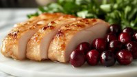 Sliced roasted duck breast with crispy golden skin served with fresh cranberries and herbs on white plate, close up view of gourmet poultry dish.