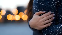 Close up of female hand with engagement ring on dark sweater against blurred bokeh lights background creating romantic winter atmosphere.