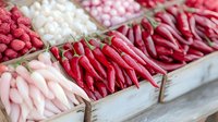Fresh red chili peppers and pink candies displayed in rustic wooden boxes at market stall, colorful food arrangement showing spicy and sweet treats.