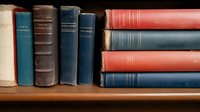 Old hardcover books arranged on wooden shelf, showing worn spines in blue, red, and white colors, creating nostalgic academic atmosphere for library or education concepts.