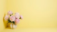 Pink peonies bouquet in white ceramic vase on yellow background with copy space, soft pastel floral home decor.