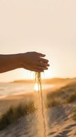Hand releasing golden sand through fingers at sunset beach with warm light creating magical moment for mindfulness and letting go concepts.