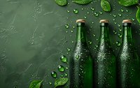 Green glass bottles with water drops and fresh mint leaves on dark textured background. Refreshing beverage concept with condensation and copy space.