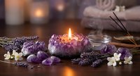 Purple amethyst crystal candle holder with burning flame surrounded by healing stones, lavender, jasmine flowers and incense sticks for spa relaxation.