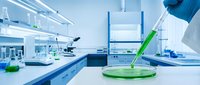 Scientist in protective gear conducting research with green liquid sample in modern laboratory with microscopes and scientific equipment for medical testing.