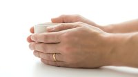 Hands holding white ceramic mug on clean background. Cozy morning coffee or tea moment with warm beverage cup. Comfort drink concept for relaxation themes.
