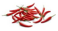 Fresh red hot chili peppers scattered on white background, spicy cayenne pods with green stems isolated for culinary design and cooking projects.