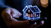 Glowing miniature house with illuminated windows held in palm at night, magical holiday decoration with sparkly blue lights creating cozy festive atmosphere.