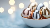 Metallic Easter eggs in white ceramic bowl against blurred bokeh background. Modern festive spring decoration with rose gold, silver and golden eggs.