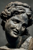 Ancient weathered stone sculpture head with curly hair showing classical artistic craftsmanship and historical cultural heritage from antiquity period.