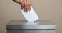 Hand placing white ballot into silver voting box during democratic election process for political campaigns and civic participation.