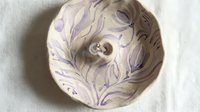 Ceramic decorative bowl featuring a female face in profile with flowing purple and lavender swirled patterns, isolated on white background for design projects.