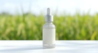Clear glass dropper bottle with white pipette on wooden surface against blurred green nature background for natural skincare and wellness products.