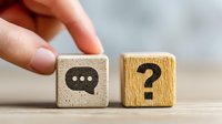 Hand placing wooden cube with chat icon next to question mark cube, representing communication and customer support concepts.