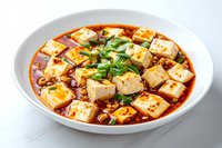 Spicy mapo tofu with minced meat in red chili sauce garnished with fresh green onions served in white ceramic bowl on light background.