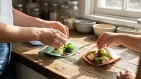 Caucasian male chef plating fresh broccoli and vegetables on ceramic dishes in bright kitchen with natural sunlight, food preparation and culinary presentation.