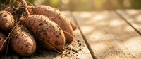 Fresh organic potatoes with soil on rustic wooden table in warm sunlight for healthy cooking and farm-to-table cuisine concepts.