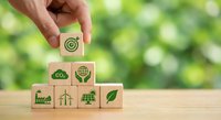 Hand placing wooden cube with target symbol on stack of eco-friendly business icons representing sustainable development goals and green solutions.