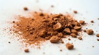 Cocoa powder and crushed cacao nibs scattered on white surface, suitable for food photography, baking, culinary, and ingredient content.