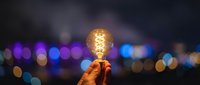 Hand holding vintage Edison bulb against blurred city lights at night. Creative inspiration and innovation concept for business presentations and marketing.