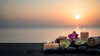 Spa wellness setup with candles, orchid flowers and towels at sunset by ocean for relaxation and meditation therapy treatments.