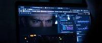Cybersecurity expert analyzing data on multiple computer monitors in dark control room with digital interface displays and security surveillance systems.