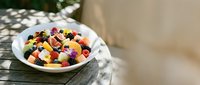 Colorful fruit salad with berries and melon served in white bowl on wooden table outdoors, perfect for healthy eating and summer dining content.
