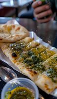 Freshly baked flatbread topped with aromatic herb oil and spices served on aluminum foil, close-up view showing crispy texture and golden-brown edges.