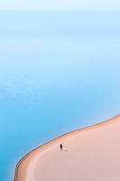 Lone silhouette walking on curved sandy dune against bright blue sky, minimalist desert landscape composition creating sense of solitude and vastness.