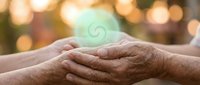 Elderly hands gently holding together with soft bokeh lights creating warm atmosphere of care, support and human connection in golden hour lighting.