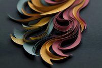 Colorful curved paper strips in gold, pink, and teal tones create dynamic abstract waves on dark background, suitable for modern design projects.
